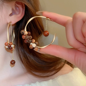 Close-up of golden C-shaped hoop earrings with woven sandalwood beads and metal chain detail