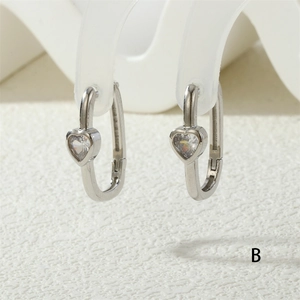 Macro detail of silver heart-shaped gemstone earrings on a minimalist white display