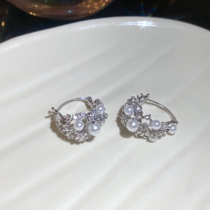 Close-up of silver flower basket earrings with pearls and shiny rhinestones on a tray