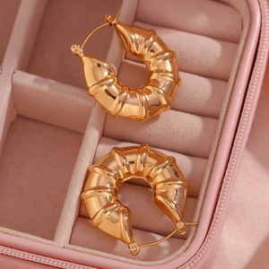 Detailed macro view of gold-plated hollow tire-shaped hoop earrings on pink velvet