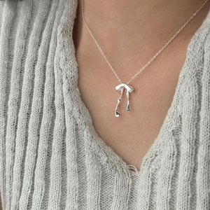 Close-up of minimalist 925 sterling silver bow necklace worn on a grey knit sweater