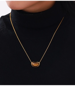 Détail d'un pendentif haricot plaqué or avec œil de tigre sur fond de pull noir chic