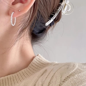 Close-up of a silver twisted hoop earring with detailed rope texture worn by a model