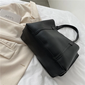 Minimalist black large capacity faux leather tote bag on white bedding with a blazer