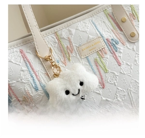 Detail of white tote bag featuring textured fabric with colorful wavy embroidery and charm