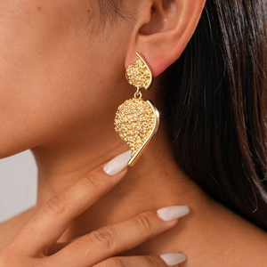 Close-up of gold metal drop earrings with irregular textures worn by a model