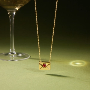 Détail du collier enveloppe en or 18 carats avec zircon coeur rouge sur fond vert olive