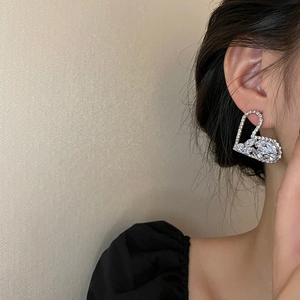 Elegant heart-shaped silver earrings with sparkling rhinestones worn by a fashion model