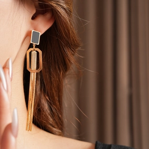 Détail de boucles d'oreilles à pompons dorés avec clou carré noir sur un mannequin