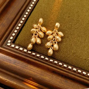 Elegant gold drop earrings with a cluster bead design on olive velvet and wood background