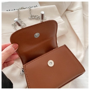 Detail view of brown leather crossbody bag featuring silver magnetic closure and chain strap
