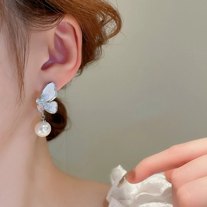Detail view of silver butterfly earring with white pearl and shell wings on female model