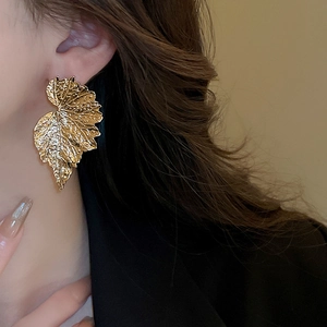 Detailed view of large gold leaf earrings with realistic vein textures on model
