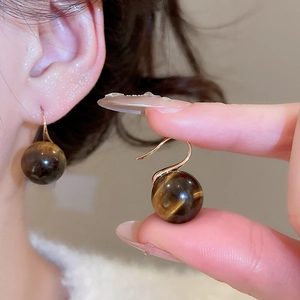 Detail of tiger eye bead earrings with golden hooks worn by a model for a luxury look