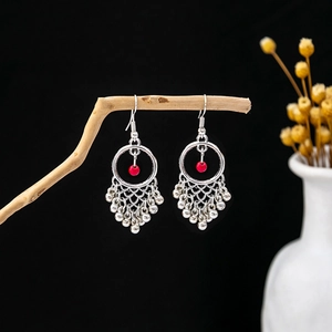 Detail of bohemian silver tassel earrings with red beads hanging on a rustic wood branch