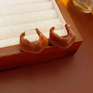 Detail view of brown flocked geometric earrings on a wooden tray with gold pins