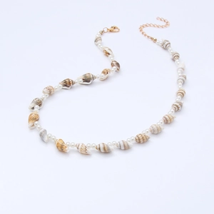 Macro detail of conch shell and white beads on a nautical necklace with gold lobster clasp