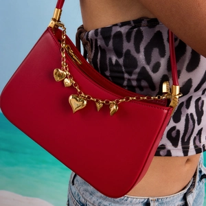 Detail of red leather baguette bag featuring golden heart charm chain on a shoulder strap