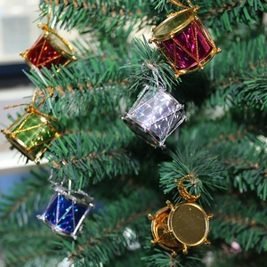 Colorful festive drum ornaments in red, gold, and blue hanging on a green Christmas tree