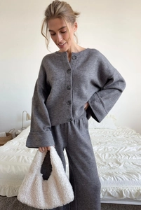 Detail of grey knitted cardigan set with round neck and soft fabric on a cozy bed background