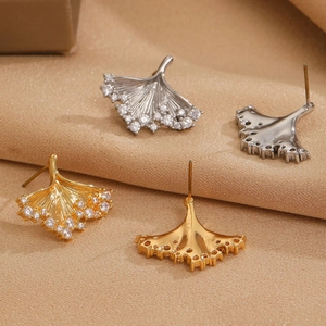 Detailed view of gold and silver ginkgo leaf stud earrings on champagne silk fabric