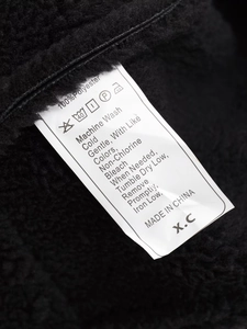 Macro shot of garment care label on black faux shearling jacket showing 100% polyester fabric