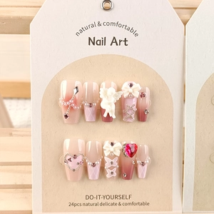 Close-up of pink gradient press-on nails with pearls, rhinestones, and bows on a card