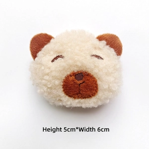 Detail of plush cream bear head accessory with embroidery, measuring 5cm high and 6cm wide