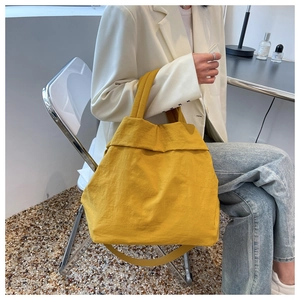 Close-up of yellow nylon tote bag with crinkled texture held by model in casual outfit