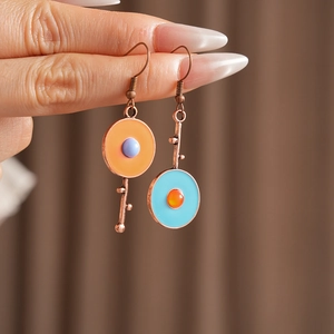 Detailed shot of vintage asymmetric enamel earrings with orange circles and key charm