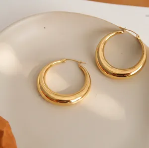 Detailed shot of gold-plated thick hoop earrings with a mirror-polished finish on a ceramic tray