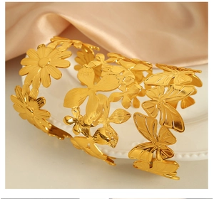 Detailed shot of gold titanium bangles with butterfly and daisy patterns on white ceramic