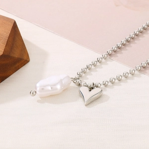 Close-up of silver bead necklace featuring a white irregular pearl and a 3D heart pendant