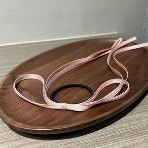 Close-up of a pink satin ribbon hair tie with a black elastic band on a wooden tray