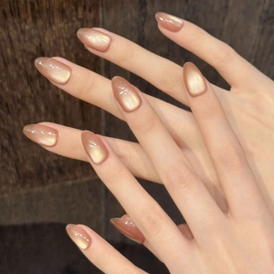 Amber gold cat eye press-on nails in long oval shape on dark wood texture background