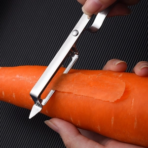Stainless steel vegetable peeler peeling a carrot over a dark textured surface