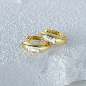 Macro shot of gold-plated square-cut crystal earrings on a textured stone background