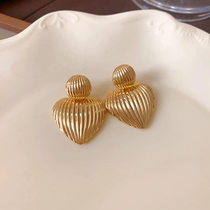 Detailansicht goldener Herzohrringe mit Streifenstruktur auf Keramikschale