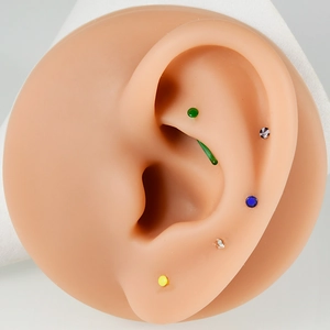 Close-up of colorful glass nose rings and ear studs displayed on a silicone ear model