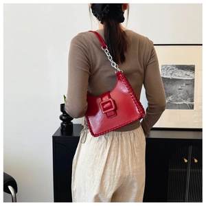 Detail of red glossy leather underarm bag featuring thick woven edges and silver chain strap