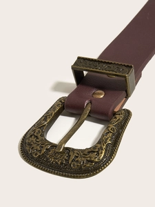 Dettaglio della fibbia vintage in bronzo con incisioni floreali su cintura marrone