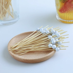 Bamboo cocktail picks with silver disco ball toppers on a round wooden tray