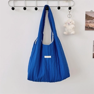 Detail of blue quilted pleated fabric shoulder bag with logo label on white wall