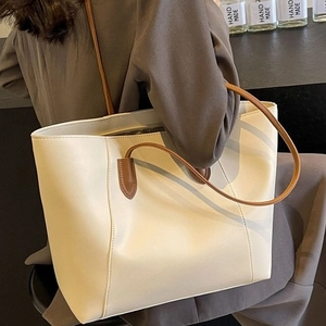 Minimalist beige tote bag with brown straps styled on shoulder over a grey blazer