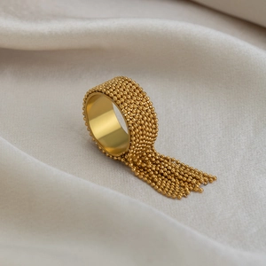 Detail of a wide gold bead ring with tassel charms on beige pleated satin background