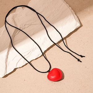 Détail du pendentif cœur en cuir rouge avec corde tissée noire sur fond de pierre