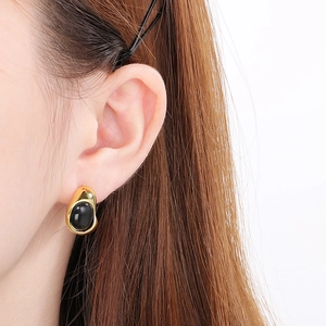 Close-up of irregular gold titanium earrings with oval black stones on a model