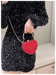 Detail of red heart-shaped evening clutch bag with crystals and gold handle on black dress