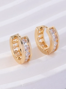 Detailed view of gold plated huggie earrings with white zirconias and hollow circular patterns
