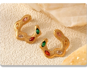 Macro shot of gold C-shape twisted earrings with colorful marquise stones and brushed finish